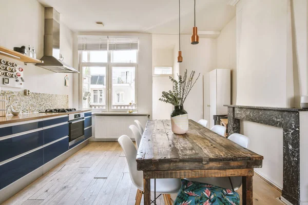 Interior of contemporary kitchen with stylish blue cupboards and appliances near dining area in contemporary apartment