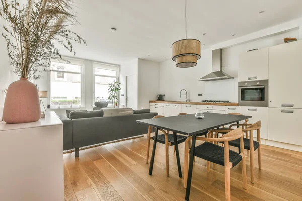 Interior of spacious light dining room with fireplace and elegant chandelier located near kitchen with modern furniture and appliances