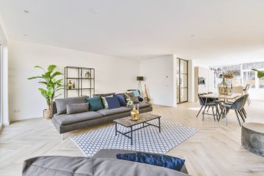 Table with chairs and flowers located under lamp against and lounge area in spacious room of modern apartment