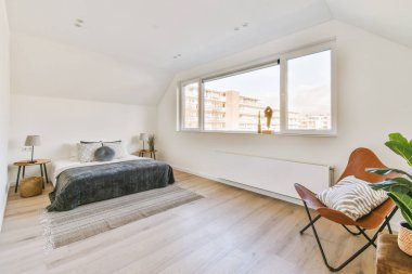 Tavan arasındaki beyaz duvarın yanında rahat bir yatak modern minimalist tarzda pencereli.