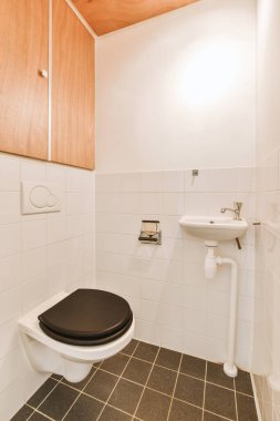 Duvara asılmış tuvalet ve köşedeki bej fayanslı lavabo.