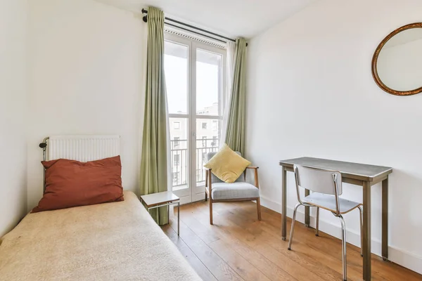 Minimalist interior design of small bedroom with soft bed placed in corner and table with shelves,armchair with lamp illumination