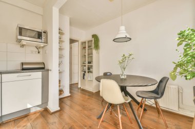 Geniş, minimalist, masa ve sandalyeli yemek odası beyaz duvarları ve ahşap zemini olan modern bir dairede.