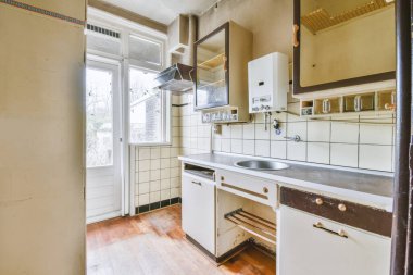 İyi organize edilmiş küçük bir ev mutfağı pencerenin altında lavabo, sobalı hafif mobilyalar ve kentsel apartmanda buzdolabı var.