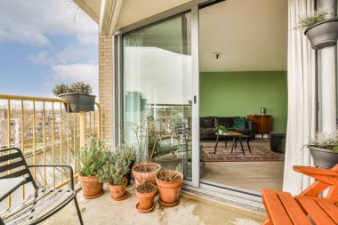 Narrow brick balcony with metal railings, wooden chair and door