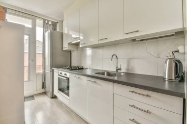İyi organize edilmiş küçük bir ev mutfağı pencerenin altında lavabo, sobalı hafif mobilyalar ve kentsel apartmanda buzdolabı var.