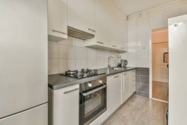 İyi organize edilmiş küçük bir ev mutfağı pencerenin altında lavabo, sobalı hafif mobilyalar ve kentsel apartmanda buzdolabı var.