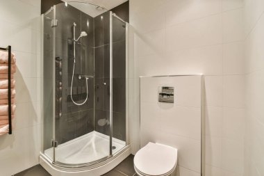 Banyonun minimalist iç kısmında duş kabini olan siyah duvar asılmış tuvalet.