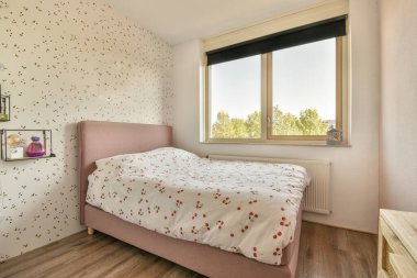 Beyaz çarşaflı rahat bir yatak ve lambasıyla pencere ve balkon kapısının yakınına yerleştirilmiş aydınlık yatak odası.