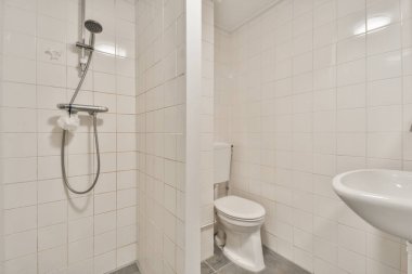 Çağdaş dairenin küçük fayanslı banyosunda lavabo ve duş arasında bulunan sifon tuvaleti