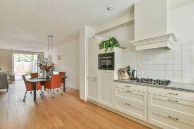 Stüdyo dairesinin modern minimalist tarzı iç tasarımı açık beyaz mutfak ve yemek masası ve sandalyeleri tavan arası lambasıyla aydınlatılmış.