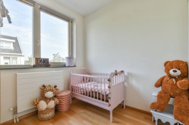 Bebek beşiği ve pencerenin yanındaki koltuğu olan beyaz odanın içi. Gün ışığında mavi çekmecelerle dolu.