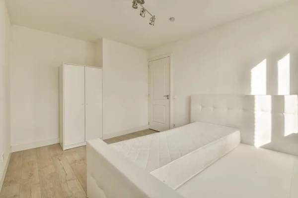 Minimalist interior design of small bedroom with soft bed placed in corner and wooden wardrobe and shelves with lamp illumination