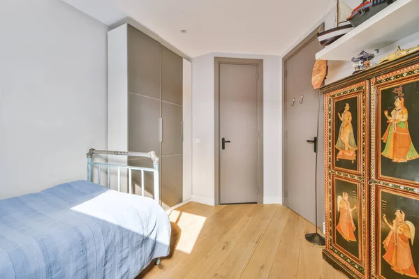 Minimalist interior design of small bedroom with soft bed placed in corner and wooden wardrobe and shelves with lamp illumination