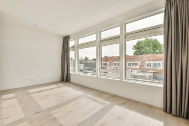 Büyük balkon pencereli, perdeli ve ahşap parke zeminli boş beyaz odanın içi.