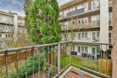 Dar tuğlalı balkon, metal parmaklıklar, tahta sandalye ve kapı.