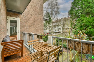 Dar tuğlalı balkon, metal parmaklıklar, tahta sandalye ve kapı.