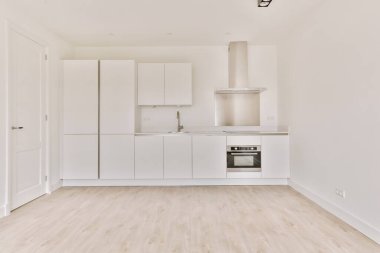 Pencereleri ve ahşap parke zemini olan boş beyaz mutfağın içi.