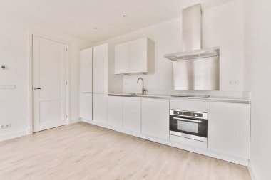 Pencereleri ve ahşap parke zemini olan boş beyaz mutfağın içi.