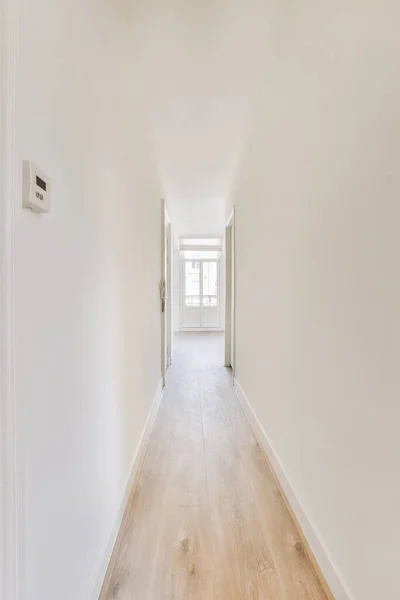 Light narrow hallway with many doors in white walls and glowing lamp over lumber floor