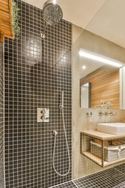 Modern banyoda aynalı lavabo ve cam kapılı duş kutusu ve beyaz fayanslı duvarlar.