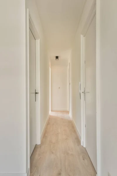 Light narrow hallway with many doors in white walls and glowing lamp over lumber floor