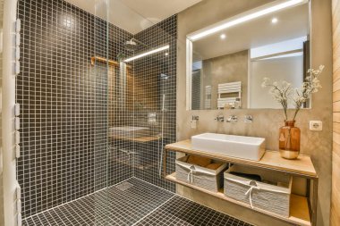 Modern banyoda aynalı lavabo ve cam kapılı duş kutusu ve beyaz fayanslı duvarlar.