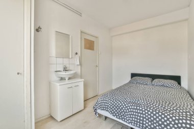 Küçük, minimalist, beyaz duvarlı yatak odasına konforlu yatak ve lamba modern dairede ayna ile batıyor.
