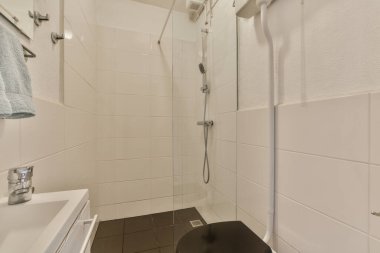 Çağdaş dairenin küçük fayanslı banyosunda lavabo ve duş arasında bulunan sifon tuvaleti