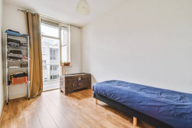 Geniş ışıklı yatak odasında beyaz yorgan ve metal raflı modern ahşap yatak.