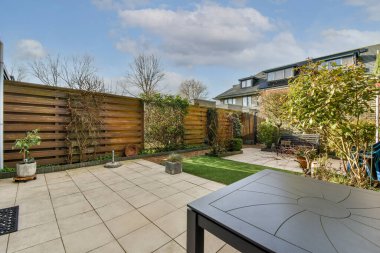 Oturma alanı ve ahşap çitlerin yanındaki küçük bahçesi olan düzgün asfaltlı bir avlu.