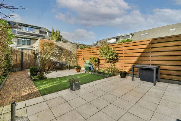 Neat paved patio with sitting area and small garden near wooden fence