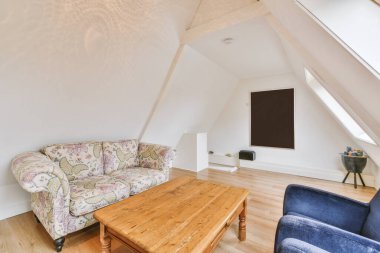 Konforlu kanepe döşenmiş oturma odasının rahat iç tasarımı ve modern tavan arası dairesinin beyaz duvarları ve sütunlarıyla döşenmiş ahşap masa.