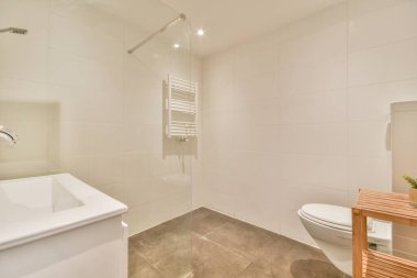 Evdeki modern tuvalette asılı duran banyo musluğu ile duvar arasındaki cam bölme.