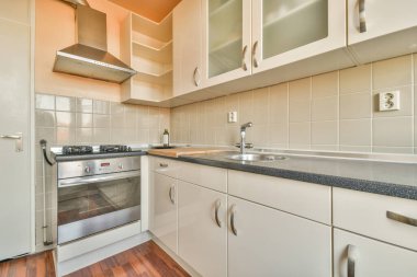 Çağdaş bir dairede, ferah bir aydınlatma mutfağında bulunan lavabo ve aletlerle aydınlatılmış dolaplar.