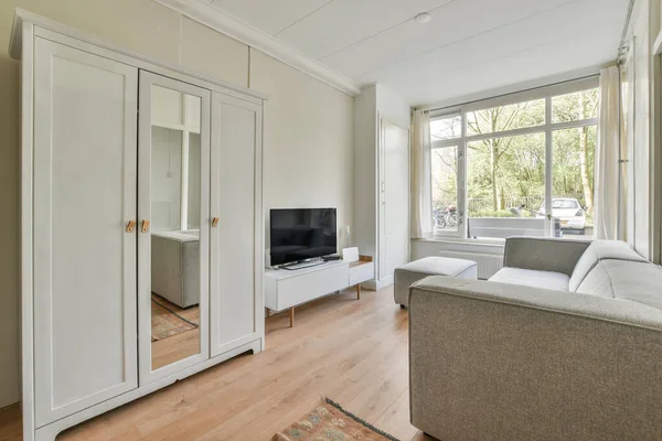 Interior of living room with comfortable sofa and TV against windows in contemporary apartment