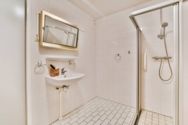 Modern banyoda aynalı lavabo ve cam kapılı duş kutusu ve beyaz fayanslı duvarlar.