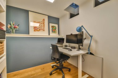 Modern apartmandaki hafif iş yerinde bilgisayar monitörleri ve beyaz tahtanın olduğu masanın yanına konforlu sandalye