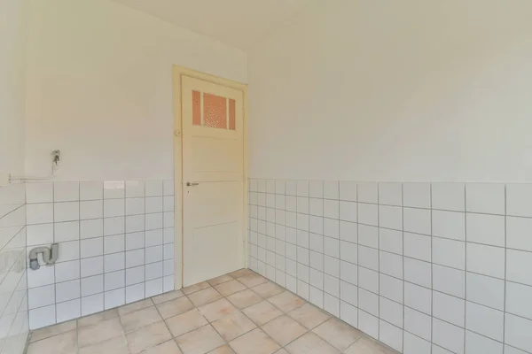Interior of empty modern apartment with geometric design with entrance door and white and tiled walls and gray tiled floor illuminated with lamp