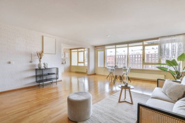 Modern bir dairede, açık mutfak ve beyaz duvarları olan, hafif mobilyaları, yumuşak koltuğu ve halısı olan şık bir iç tasarım.