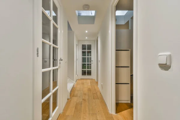 Light narrow hallway with many doors in white walls and glowing lamp over lumber floor