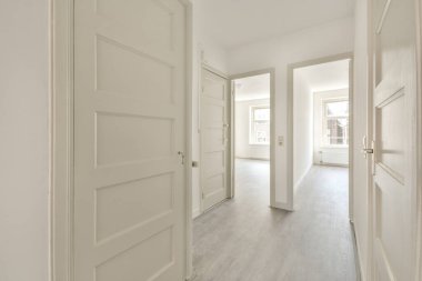 Beyaz duvarları ve kapıları olan dar koridor modern dairede pencereleri ve parke zemini olan geniş odaya açılıyor.