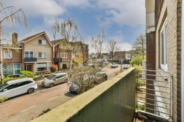 Arabaları, ağaçları ve fenerleri olan boş bir kaldırımdan panorama manzaralı evler.