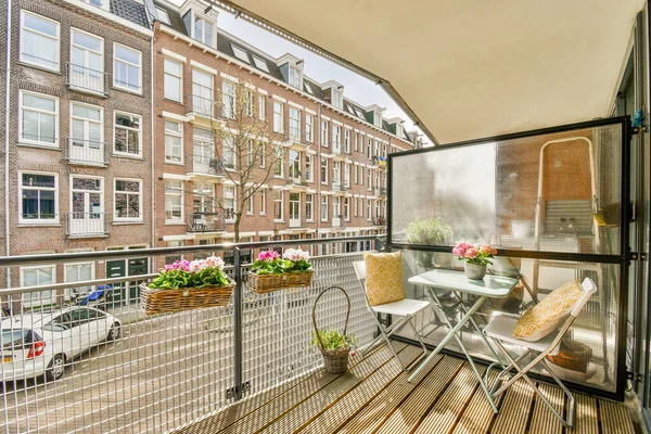 Dar tuğlalı balkon, metal parmaklıklar, tahta sandalye ve kapı.