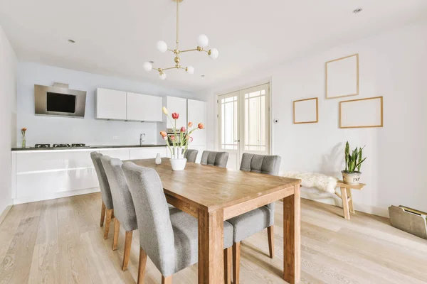 Modern minimalist style interior design of studio apartment with open white kitchen and dining zone with table and chairs illuminated by loft style lamp