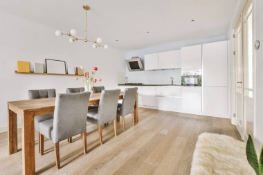 Stüdyo dairesinin modern minimalist tarzı iç tasarımı açık beyaz mutfak ve yemek masası ve sandalyeleri tavan arası lambasıyla aydınlatılmış.