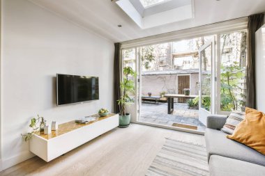 Çağdaş dairenin pencerelerine karşı rahat kanepesi ve televizyonu olan oturma odası.