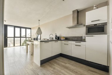 Beyaz oturma odasında açık siyah mutfak, yemek masası ve gri kanepe.