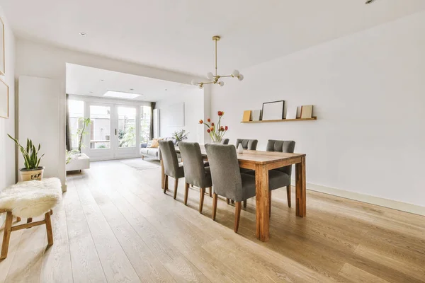 Modern minimalist style interior design of studio apartment with open white kitchen and dining zone with table and chairs illuminated by loft style lamp