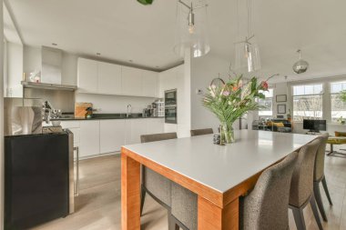 Stüdyo dairesinin modern minimalist tarzı iç tasarımı açık beyaz mutfak ve yemek masası ve sandalyeleri tavan arası lambasıyla aydınlatılmış.